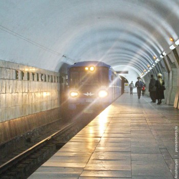 Перрон, название станции на путевой стене и приближающийся поезд.